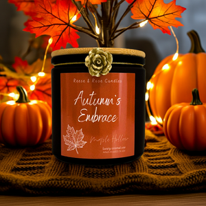 Candle labeled 'Autumn's Embrace' with pumpkins and leaves on a dark background